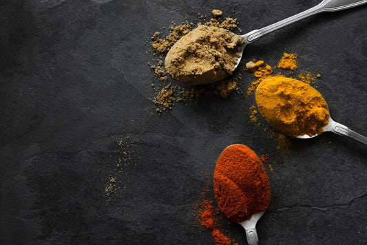 three spoons containing spice powders of brown, yellow and red powders